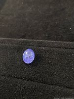 Oval blue-violet tanzanite resting on black surface