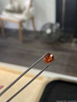 Oval spessartite garnet held in tweezers showing overall size and colour