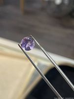 Round brilliant cut amethyst held by tweezers