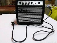 Front view of black Carlson EGA30 guitar amplifier showing four control knobs, speaker grille, power switch, and attached power cord laid out on a white surface.