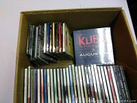 Box containing a range of CD cases with visible titles inspired by pop, classical, and movie music.