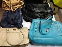 Four large handbags displayed on a surface showing colors tan, navy blue, black, and turquoise with different styles and features.