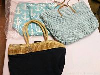 Three summer beach purses with distinct styles: a large woven tote in light blue, a blue and tan handbag with nautical detail, and a blue anchor print pouch in plastic wrapping.