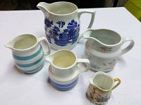 Front view of five ceramic pitchers grouped together on a white surface showing various floral and striped patterns.
