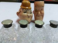 Front view of the six salt and pepper shakers, showing two character heads and four cut glass shakers with silver tops