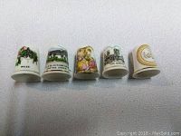 Front view of the five bone china thimbles showing various scenic and floral decorations.