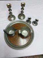 Photo showing two large pewter candlesticks, two small pewter candlesticks, a creamer, a sugar bowl, all on a large pewter tray with wooden center.
