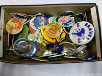 Top-down view of a box filled with assorted pinback buttons showing various logos and cartoon images.