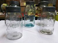Five vintage glass jars displayed on white surface, including three Ball jars and two Crown Ball jars with black lids.