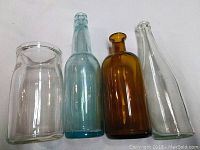 Four old glass bottles side by side: clear, blue, amber, and clear for color and shape comparison.