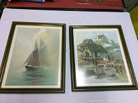 Two framed Degarthe prints on a flat surface showing scenes of sailboat and Peggys Cove buildings.