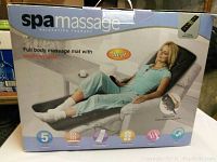 Front view of the SpaMassage branded box showing product image of a woman using the full body massage mat with heat features and remote control.