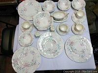 Top view of the china set arranged on a white cloth, showing plates, bowls, cups, saucers, gravy boat, and shakers with pastel floral pattern.