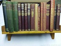 Photo of antique classic books with titles including Our Mutual Friend, The Rainbow, Cranford, and others arranged on a wooden book stand.