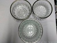Three glass serving bowls viewed from above showing silver rims and intricate patterns inside.