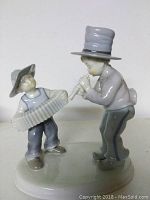 Porcelain figurine showing two boys playing musical instruments; one with accordion and the other with flute, standing on a shared base.