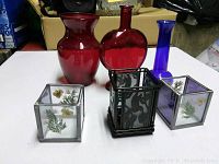 Lot shows three glass vases (two red, one blue) and three candle holders on a white surface.