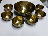 Top view of one large and six smaller hammered brass-finish bowls arranged on a white surface