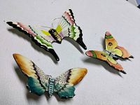 Three hand-painted ceramic butterflies displayed showing top view with detailed colors and patterns