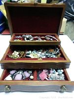 Wooden jewelry box with three open drawers revealing assorted costume jewelry inside compartments lined with red velvet.