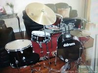 Full kit assembled in living room showing red bass drum with Ddrum logo, rack toms, floor tom, snare on stand, cymbals and pedal.