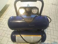 Front and top view of Campbell Hausfeld air compressor showing blue cylindrical tanks, black padded handle, pressure gauges, and control knob.