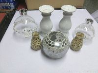 Photo of the full lot showing all seven candle holders arranged on a table, including two white ceramic pillars, two clear bead-accented glass dome holders, two small gold honeycomb mosaic holders, and one large silver mosaic spherical holder.