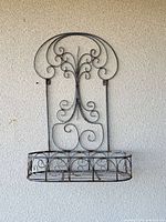Front view of wrought iron wall planter showing full scroll design and basket