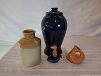 Front view of the three vessels: blue urn with spigot and drip dish, stoneware jar, peach vase