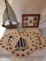 Lot overview showing metal sailboat decor, glass vase, framed print, and wool sailboat mats