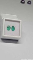 Pair of oval emeralds in display box, frontal view