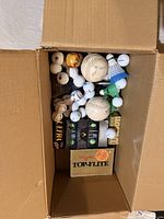 Open carton containing mixed loose and boxed golf balls, baseballs and shuttlecocks