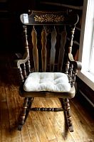 Front view of the dark wood rocking chair with floral detail on backrest and tufted seat cushion