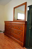 Front view of six-drawer wood dresser with attached rectangular mirror in honey finish