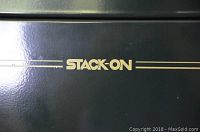 Close-up of front door showing gold Stack-On logo on green powder-coat finish.