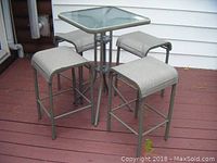 Full view of the square glass top table with 4 stools arranged around it on a deck.