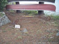 Red fibreglass canoe hung upside down between trees, showing length and general wear
