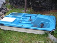 Blue and white fibreglass pedal boat viewed from starboard side showing top deck, seat recesses, steering tiller and metal pedal mechanism