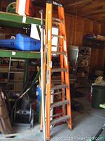 Orange aluminum step ladder standing in a garage with various equipment around.