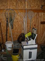 Set of fishing nets with metal and wooden handles leaning against wooden wall; Styrofoam cooler and bucket also visible in the background.