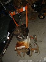 Full view of AMF gas-powered tiller showing the orange frame, engine, and tilling blades with rust.