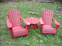 Two red vintage wooden Muskoka chairs with matching small round table outdoors on grass.