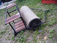 Lawn roller lying on its side next to BBQ frame on grass
