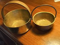 Two brass buckets on tabletop showing size difference and patina