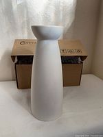 Front view of white ceramic vase standing in front of packing box