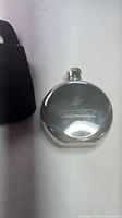 Front view of Rémy Martin round stainless steel flask with screw cap and partial view of black velvet pouch