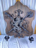 Full view of wood backboard with cast iron scrollwork, crossed axe and halberd, lion crest, and candle holders