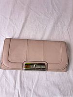 Full view of closed blush leather Coach wallet showing turn-lock clasp and overall condition