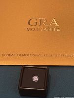 Round moissanite in black box beside gold GRA folder