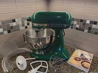 Green KitchenAid stand mixer with bowl, shield, paddle, whisk, dough hook, recipe book on countertop